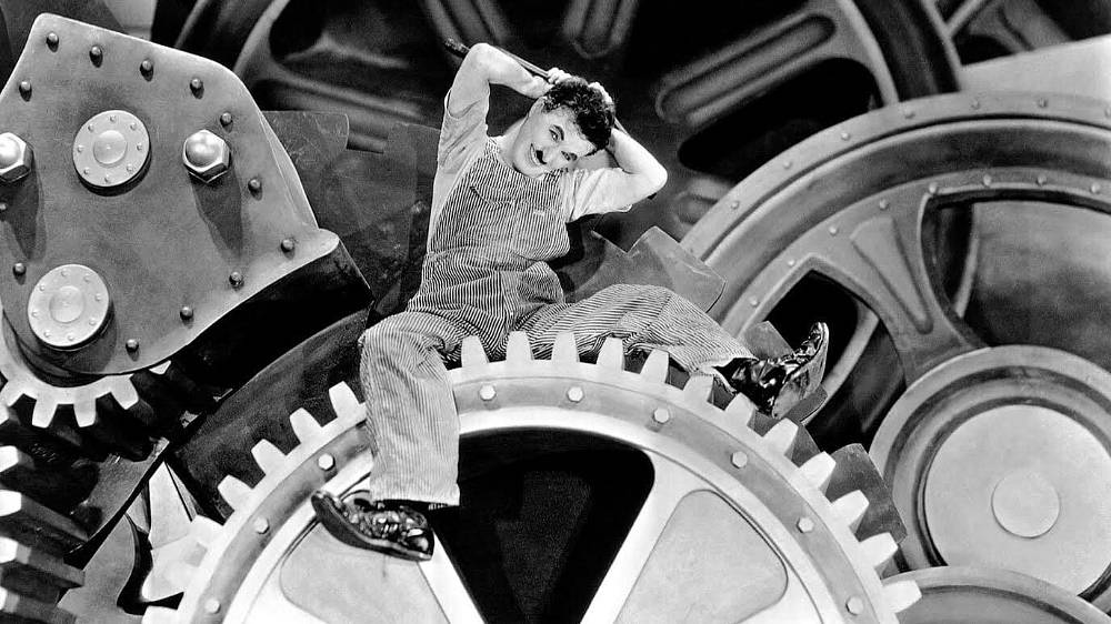 Moderní doba. Charles Chaplin a jeho souboj se stroji v éře, která není příliš nakloněna lidem. Společenská satira natáčená ještě v konvencích pantomimy němého období. Protest proti nehumánním aspektům technické civilizace a automatizace lidského života. Film je vybudovaný jako mozaika epizod, každá z nich má vlastní výstavbu gagů, geniálně se v ní uplatňuje smysl pro humor ironii i sarkasmus.