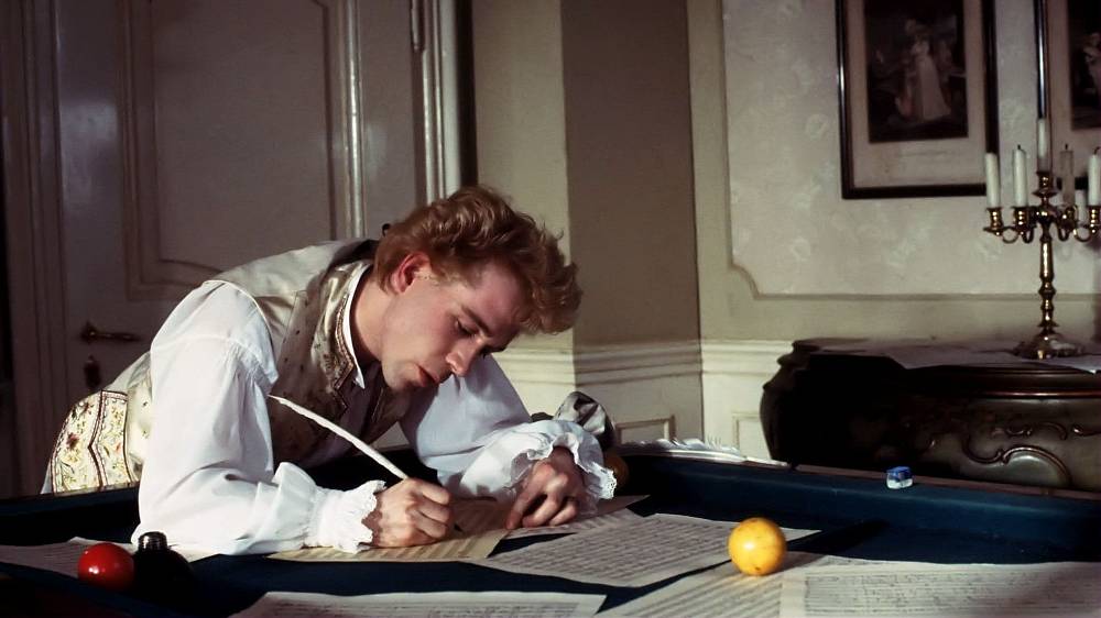 Amadeus. Strhující drama závisti, žárlivosti, intrik a vášnivé lásky k hudbě. Jeden z nejlepších filmů historie, oceněný osmi Oscary, mj. i za kostýmy Theodora Pištěka.
Český režisér Miloš Forman našel během svého amerického působení osobní téma v zápase výjimečného jedince s představiteli politické i jiné moci. Ideální látku objevil v divadelní hře Petera Shaffera Amadeus, která se od svého uvedení v roce 1981 stala hitem světových scén. Geniální skladatel Wolfgang Amadeus Mozart se v ní stane obětí vražedných intrik svého kolegy, dvorního skladatele Antonia Salieriho, jenž nedovede unést tíhu závisti a vlastní průměrnosti. Právě Salieri je – navzdory titulu – hlavním hrdinou divadelního i filmového příběhu. Skladatel, posedlý touhou po uznání a slávě, kvůli splnění svých snů uzavře smlouvu s Bohem. Ten však zbožnému komponistovi nadělí jen průměrné hudební nadání. Geniálními schopnostmi naopak obdaří samolibého, nevycválaného a nafoukaného hejska jménem Mozart. Salieri se chce Bohu za tuto zradu pomstít tím, že jeho miláčka zprovodí ze světa... Miloš Forman natočil podle Shafferova scénáře naprosto výjimečné filmové dílo, jež ve své době zaznamenalo neočekávaný divácký úspěch a způsobilo dokonce „mozartománii". Ve skvěle vystavěných dramatických scénách totiž Forman brilantním způsobem využil právě roli hudby. Amadeus získal mimo řady jiných prestižních ocenění také osm Oscarů: jako nejlepší film, dále za režii, za mužský herecký výkon v hlavní roli (F. Murray Abraham), za scénář podle předlohy, výpravu, kostýmy (T. Pištěk), masky a zvuk. Neproměněná zůstala druhá nominace za hlavní mužskou roli (Tom Hulce), za kameru (Miroslav Ondříček) a za střih.
