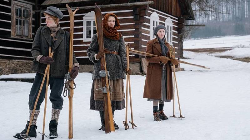 Záběr z filmu: děti s lyžemi před chalupou